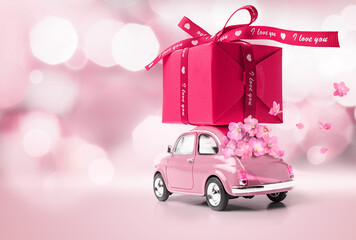 Pink car delivering red gift box and flowers on pink background. Copy space.