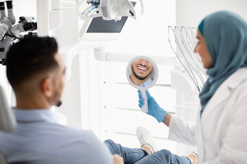 Arab Male Patient Looking At His Smile After Treatment In Dental Clinic