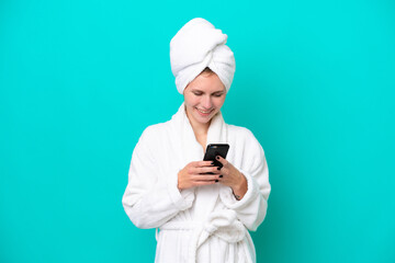 Young woman in a bathrobe isolated on blue background sending a message with the mobile