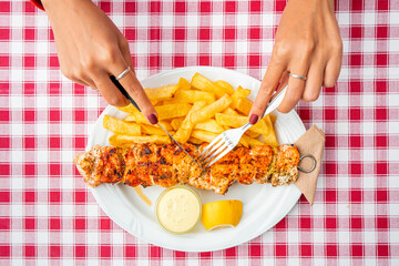 A girl using a knife and fork to eat traditional Greek grilled meat - souvlaki with french fries. Fastfood and healthy diet concept