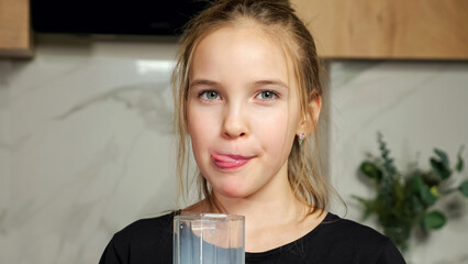 Teenage girl in black t-shirt drinks fresh milk from glass licking white mustache on upper lip standing against marble wall in kitchen closeup. - obrazy, fototapety, plakaty