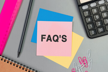 FAQ - frequently asked questions - text on sticky note. Top view image of pink card, pencil, calculator and with many paper clips on table. Flat lay design