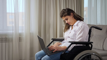 Young disabled long haired woman with cerebral palsy works online remotely via laptop sitting in...