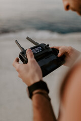 young male traveller is using drone to film and photograph aerial views of a beach in Greece, surrounded by rocky white cliffs and blue water at sunset