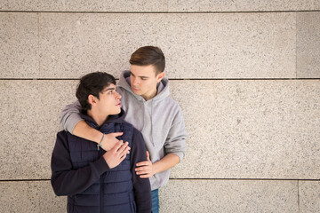 portrait of a young homosexual couple looking at each other on a gray wall background