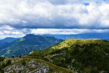 View of Julian alps in Gorenjska, Slovenia and Ratitovec mountain range with forest covering the base and meadow at the top