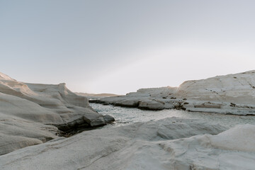 The sandstone white rocks cliffs moonscape of Sarakiniki volcanic beach in Milos Island Greece surrounded by turquoise blue waves and sea at sunset