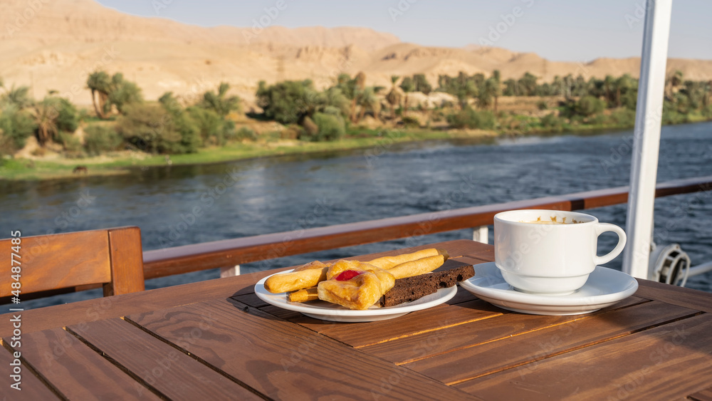 Wall mural the deck of a cruise ship. on a wooden table there is a cup of coffee and a saucer with pastries, cu