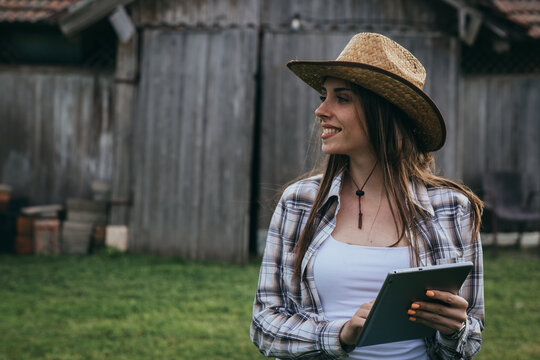 woman farmer using digital tablet in front of wooden barn