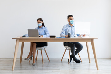 Colleagues in disposable face masks working on pc at office
