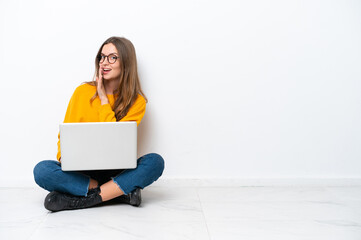 Young caucasian woman with a laptop sitting on the floor isolated on white background whispering...