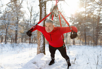 Athletic senior man doing bungee fitness exercises, training outdoors on sunny winter morning
