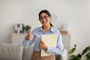 Positive female psychologist gesturing thumb up, working in office and smiling, recommending...