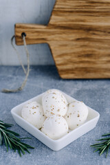Fresh soft Italian white cheese mozzarella buffalo in white bowl served with fresh rosemary branch