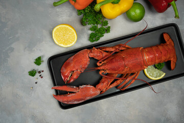 Lobster decorated with lemon slices on black plate on concrete table. Fresh seafood.