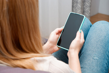 A woman at home sitting on the couch communicates with relatives via video call using a smartphone. Young woman making video call with her family