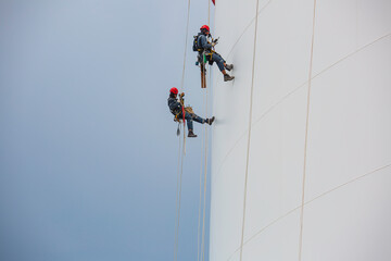 Male workers control rope down height tank rope access inspection of thickness shell plate tank.