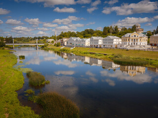 Fototapeta premium summer travel to Russia, Torzhok city, Tver region. View on old buildings at the embankment from the bridge across the Tvertsa river. Rural landscape