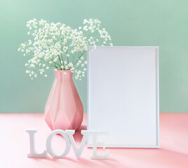 Creative card with gypsophila in vase, empty white frame, white letters LOVE on pastel pink-green.