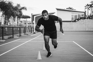 Hispanic man doing speed and agility cone drills workout session outdoors - Focus on man face -...