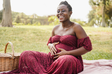 Young african pregnant woman touching her belly outdoor at city park - Focus on face