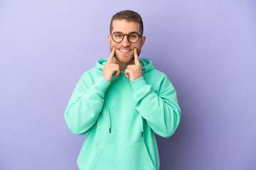 Young handsome caucasian man isolated on purple background smiling with a happy and pleasant expression