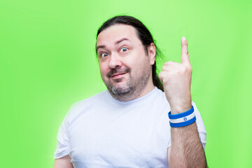 An adult, unshaven man in a T-shirt points his finger up. Bracelet in the colors of the flag of Israel.