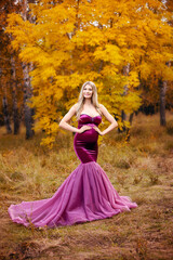 beautiful pregnant blonde woman with long hair in a purple long dress on the background of an autumn forest