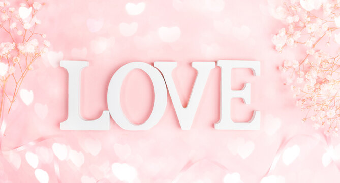 White letters LOVE with frame of gentle white gipsofila on pastel pink with bokeh lights hearts.