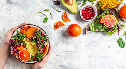 Fototapeta na wymiar Healthy vegetarian buddha bowl salad with avocado, persimmon, blood orange, nuts, spinach, arugula and pomegranate on a light background, Long banner format, top view