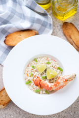 Risotto with crab meat served in a white plate with baguette, vertical shot on a beige marble background, high angle view