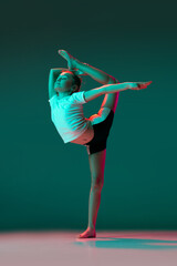 Little flexible girl, rhythmic gymnastics artist training isolated on green studio background in...