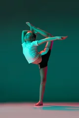 Poster Im Rahmen Little flexible girl, rhythmic gymnastics artist training isolated on green studio background in neon pink light. Grace in motion, action. Doing exercises in flexibility. © master1305