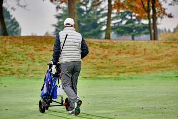 Golfer on a golf course in winter with frost covering the grass, pushing the cart up to the ball.