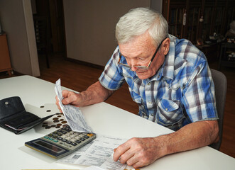 Upset Senior man sitting at the table and calculating finances. Old man checking bills. Man counting coins on the table. Pension calculation concept