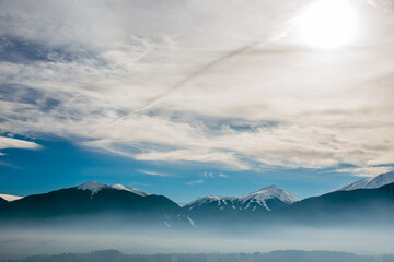 Pirin mountain, Bulgaria. Covered in snow peak in winter skiing season. Mist fog below the mountain. Blue cloudy sky.