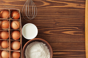 Ingredients for baking - flour, eggs, milk. With rolling pin, whip and pouch. On wooden table