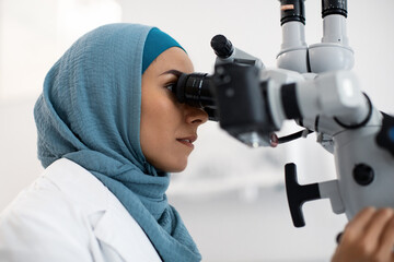 Muslim Female Medical Worker In Hijab Using Dental Microscope In Modern Clinic