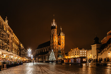 Krakow,Poland.Basilica of Saint Mary and famous Christmas market on main square,Rynek Glowny at night,decorated timber huts and Xmas tree.People enjoying festive atmosphere,blurred people in motion.