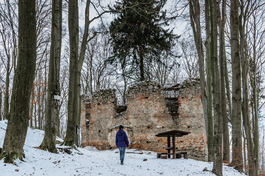 Hiking girl enjoying view of ruins of abandoned Chapel of Saint Mary Magdalene on hill of Maly Blanik,Czech Republic.Pilgrimage place with great spruce growing within chapel walls.Snowy winter day