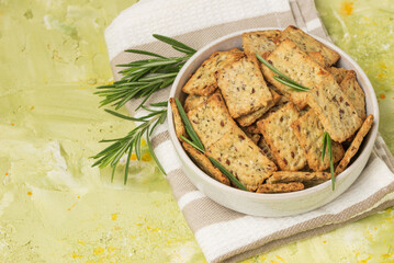 Homemade diet cookies with herbs, flax seeds and spices  in a light plate on  green table. Crunchy rosemary crackers top view, close up plan