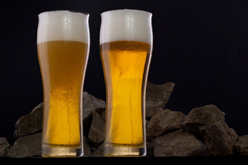 Couple of glasses of fresh and cold beer in a dark set decorated with rocks