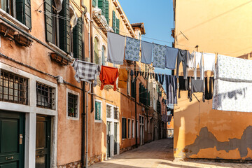 Fototapeta na wymiar Laundry hanging out of typical Venetian facade,Italy.Narrow street with colorful buildings and clothes dry on rope,Venice.Clean clothes drying outdoors in small square.City lifestyle,urban scene.