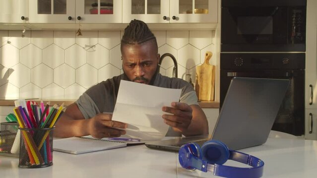 Shocked upset stylish good looking African American man calculating finance, receiving eviction notice and grabbing head with hands, expressing despair and frustration in domestic kitchen.