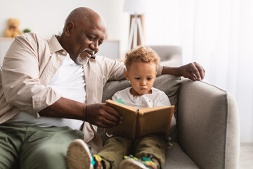 African American Grandfather And Little Grandson Reading Book At Home