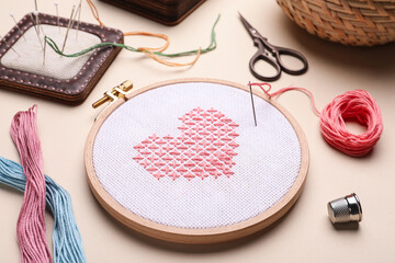 Embroidery and different sewing accessories on beige background