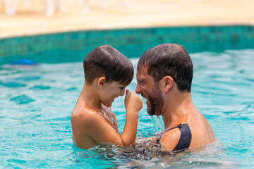 Father plays with his son in the pool, both are laughing as they get out of the bottom of the pool