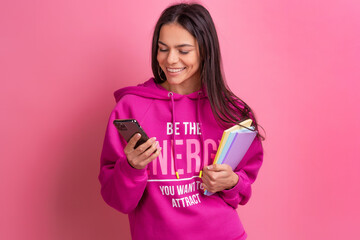 hispanic pretty woman in pink hoodie smiling holding holding notebooks and using smartphone