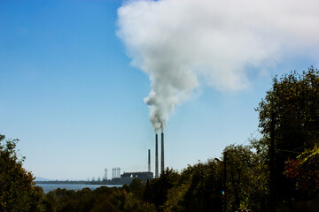 Chimney with smoke coming out of it against a blue sky in the industrial area. Environmental...