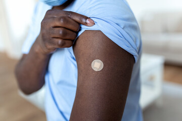 African man holding up his shirt sleeve and showing his arm with bandage after receiving vaccination. covid 19 immunization